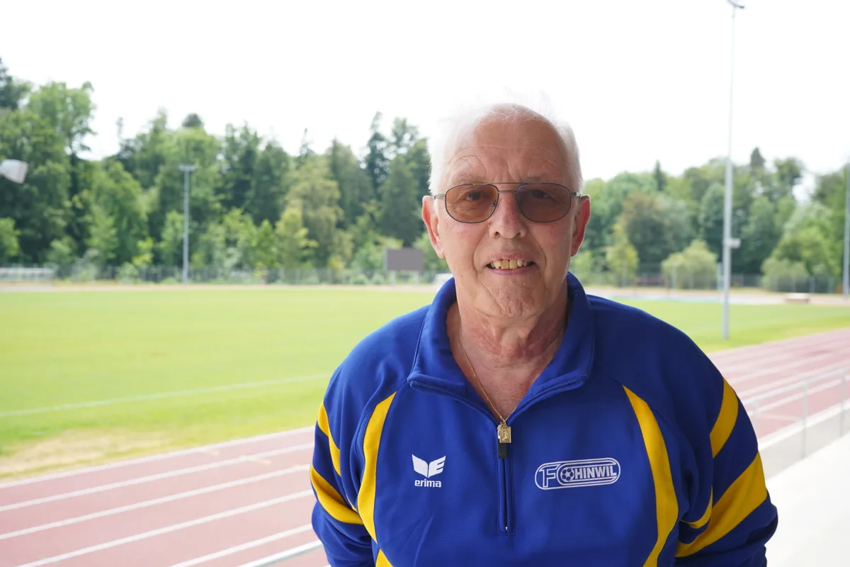 Ein Mann in einem blau-gelben FC-Hinwil-Trainer posiert auf einem Sportplatz.
